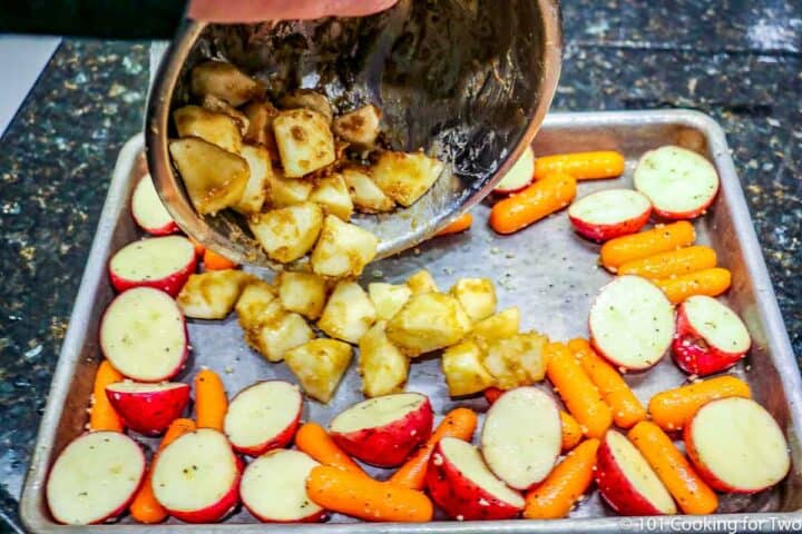 pouring coated apple onto tray with carrots and potatoes