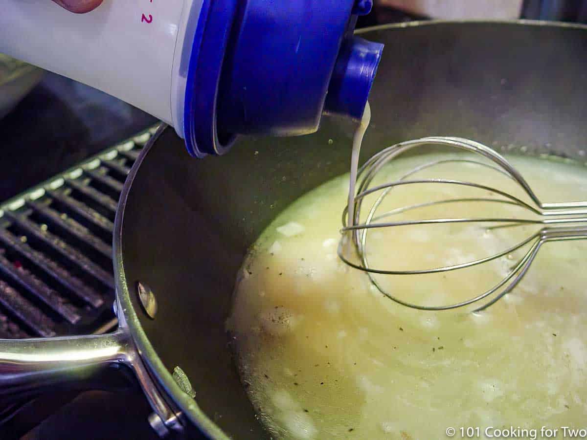 pouring flour mixture into broth with whisk