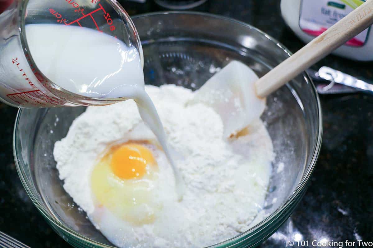 pouring milk into bowl with flour and egg