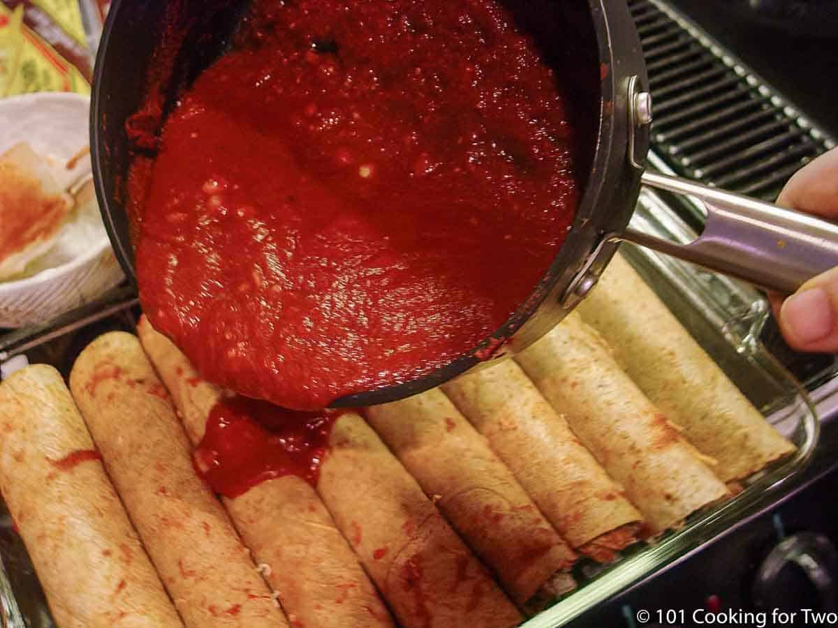 pouring red enchilada sauce over chicken enchiladas