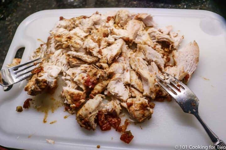 shredding chicken on a white board with forks