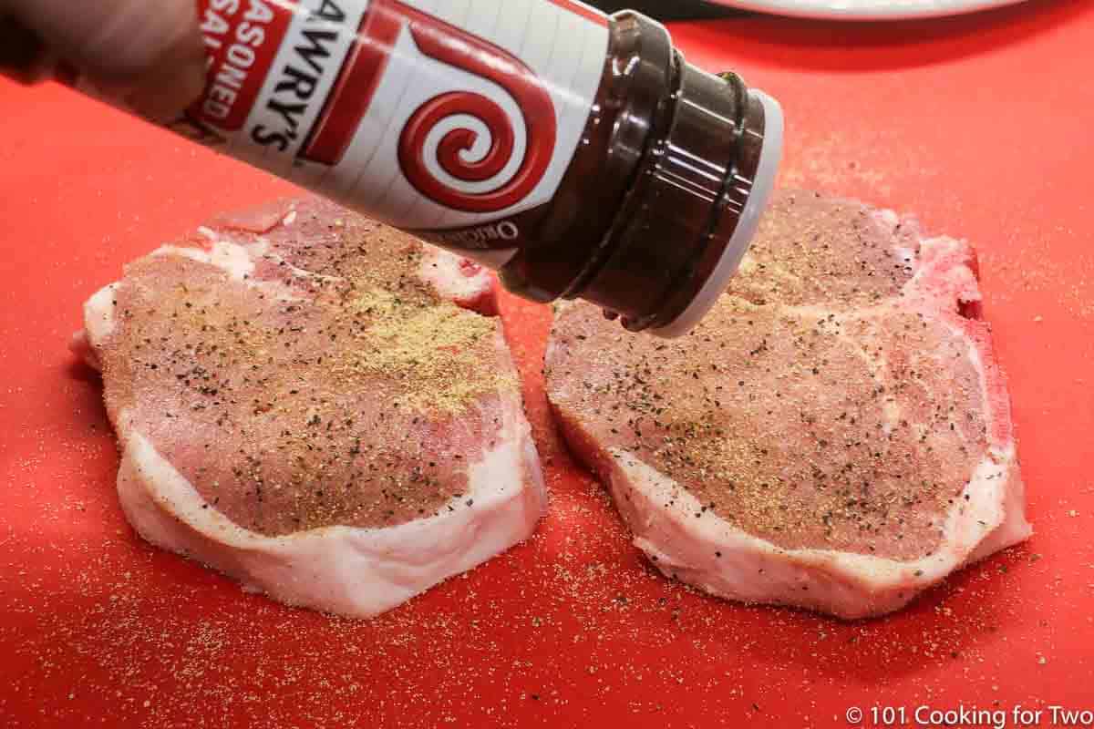 sprinkling seasoning salt on pork chops.