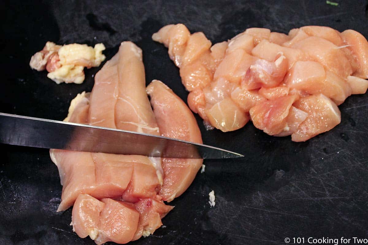 cutting chicken breasts into cubes on a black board.