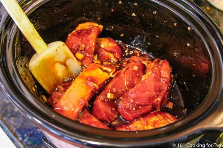 mixing pork ribs into the sauce in a crock pot