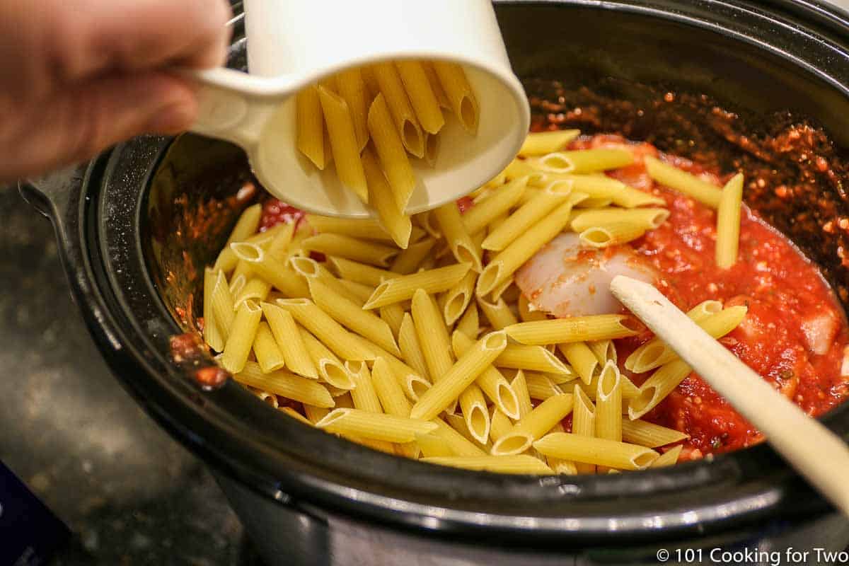 pouring dry pasta into the crock pot with sauce