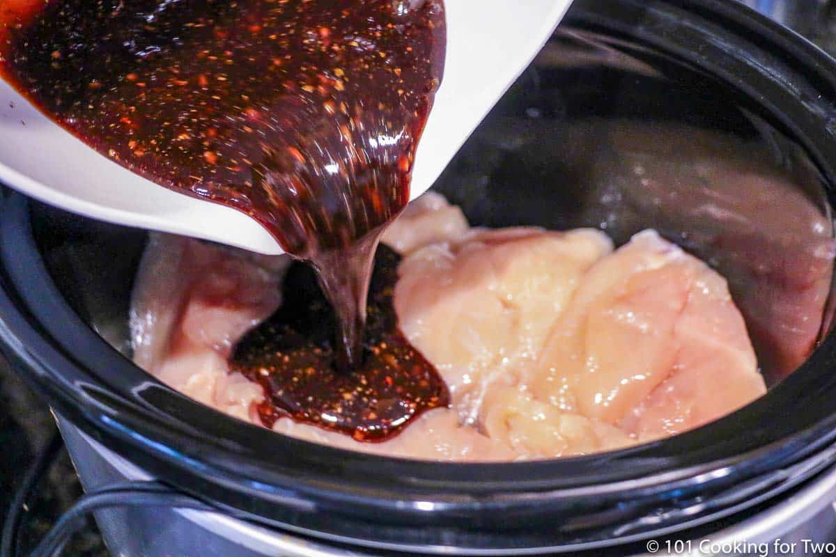 Pouring sauce over raw chicken in the crock pot.