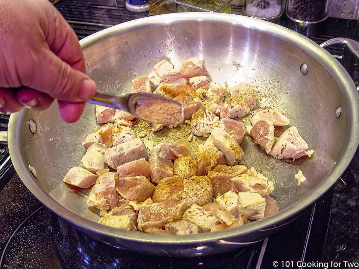 sprinkling spices over browning chicken in fry pan