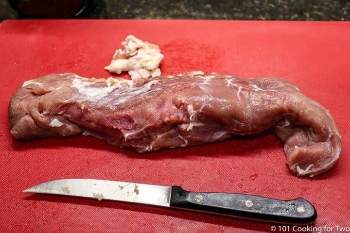 trimmed pork tenderloin on a red board with a knife