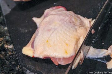 trimming chicken thigh on a black board