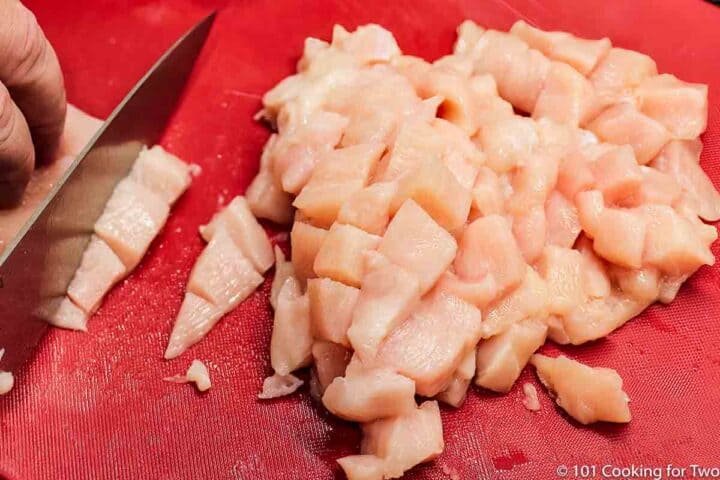 trimming raw chicken into cubes
