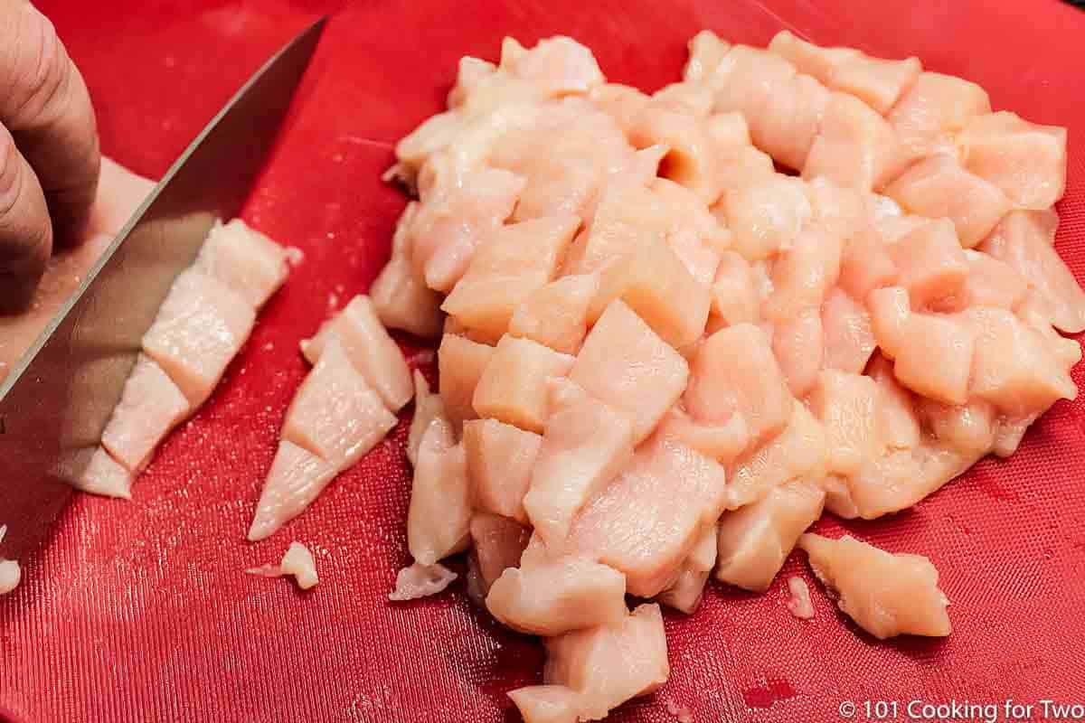 trimming raw chicken into cubes.