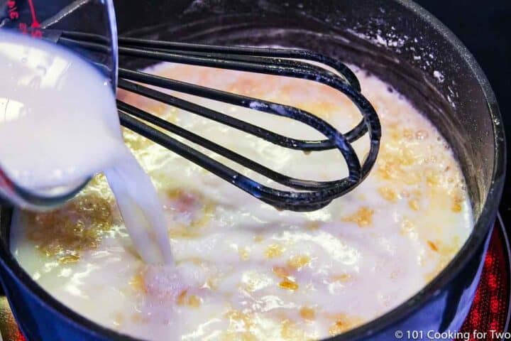 adding milk to roux with whisk in sauce pan