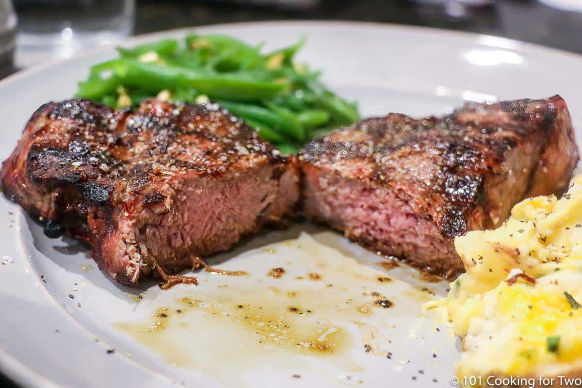 cut strip steak on a gray plate with potatoes and beans.