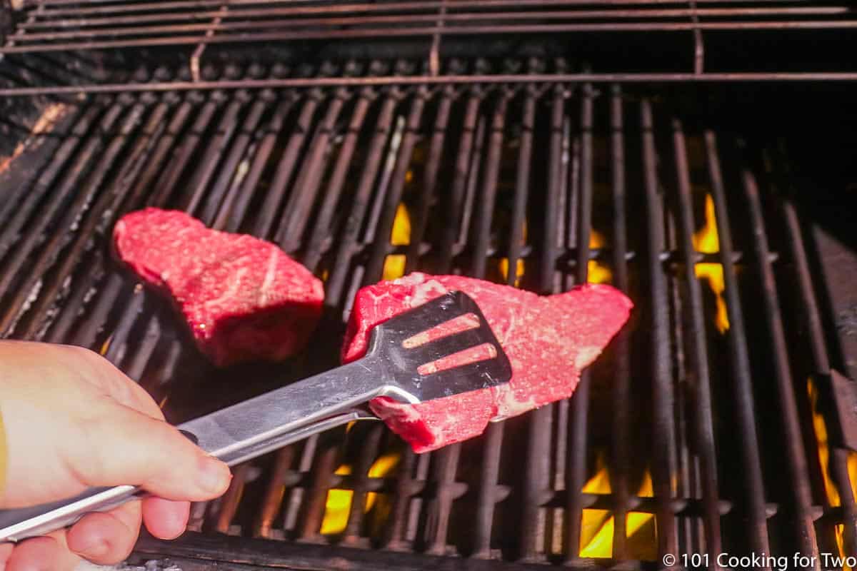 placing strip steak on the grill grate.