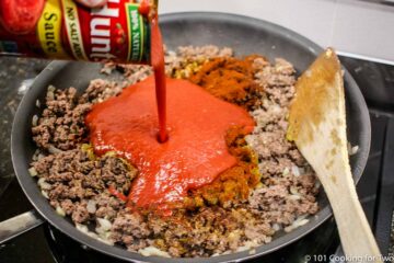 pouring tomato sauce into pan with cooked ground meat