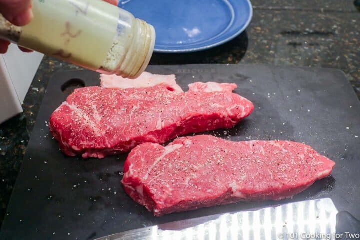 seasoning strip steaks on a black board