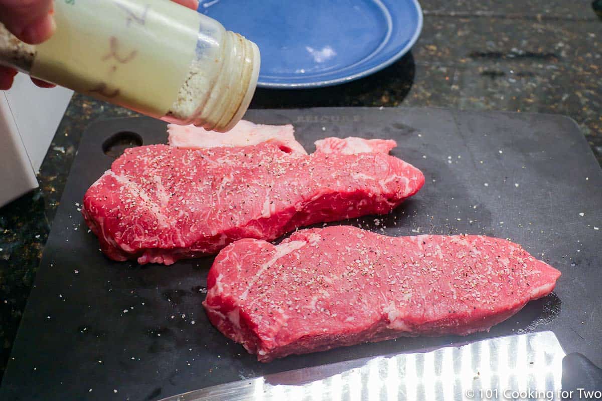 seasoning strip steaks on a black board.