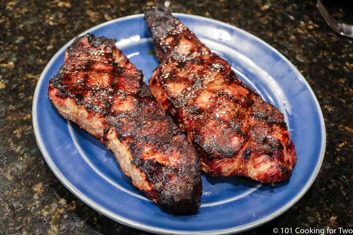 two grilled strip steaks on a blue plate.