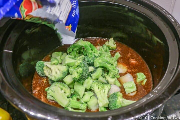 adding frozen broccoli to the cooked meat in the crock pot