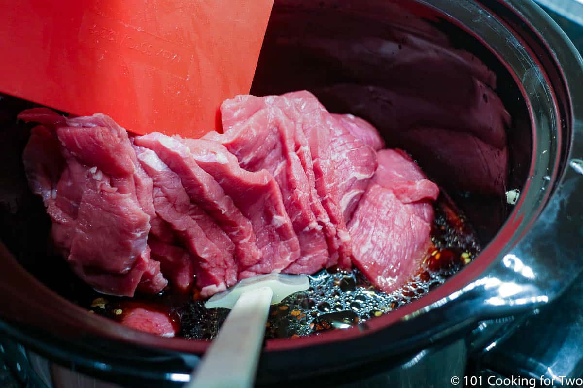 adding sliced beef to the crock pot.