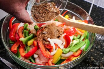 adding spices to bowl of veggies and chicken
