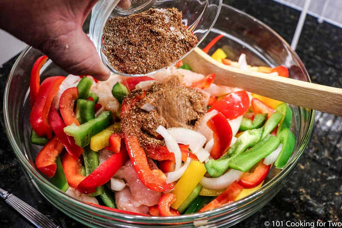 adding spices to bowl of veggies and chicken.