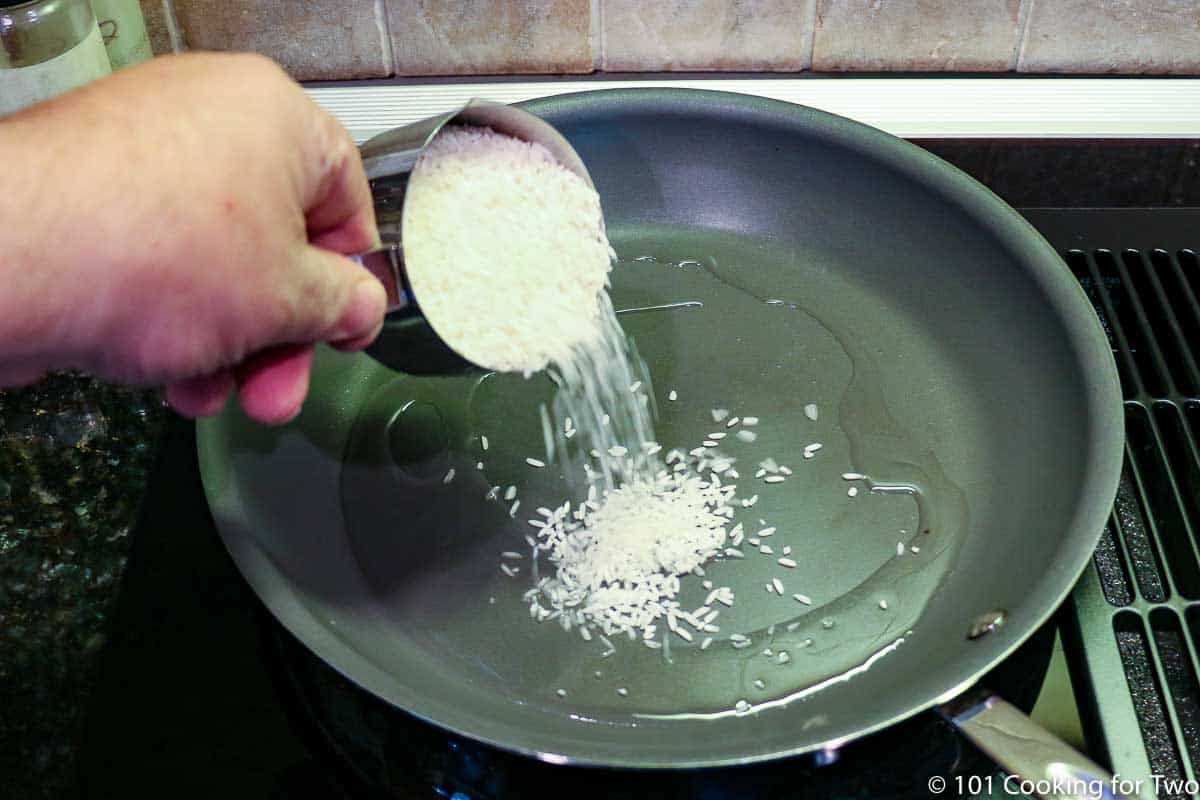 adding uncooked rice to hot oil in a skillet