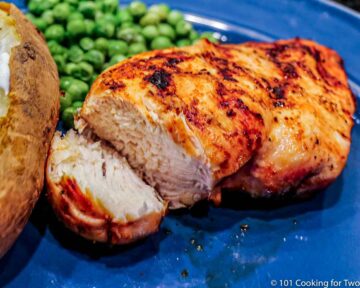 cut chicken breast on blue plate with potato and peas