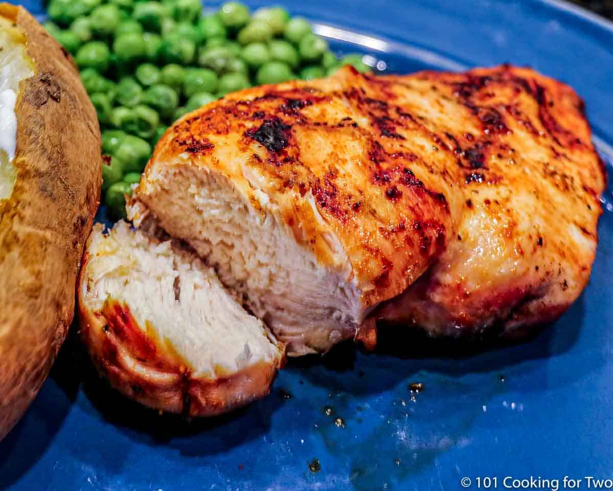 cut chicken breast on blue plate with potato and peas.