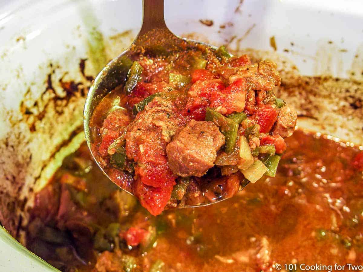 ladle of cooked chili over a crock pot.