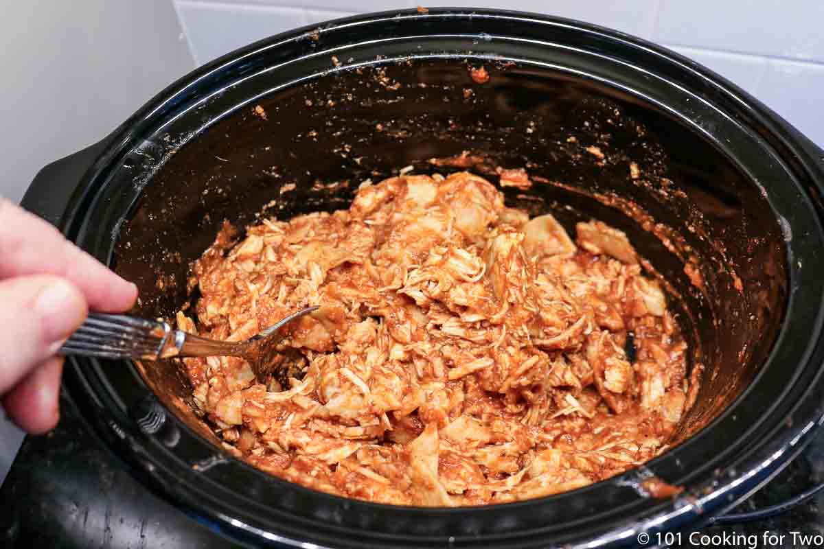 mixing shredded chicken into the sauce.