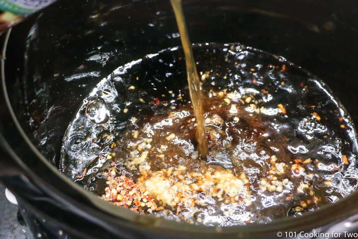pouring beef broth into crock pot with other ingredients.