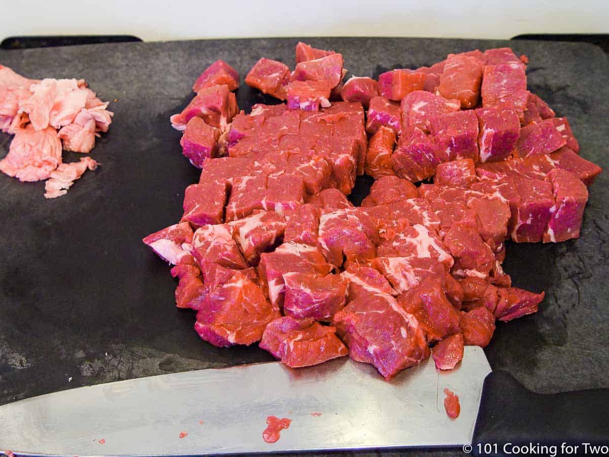 raw chuck roast trimmed and cut into cubes on black board.