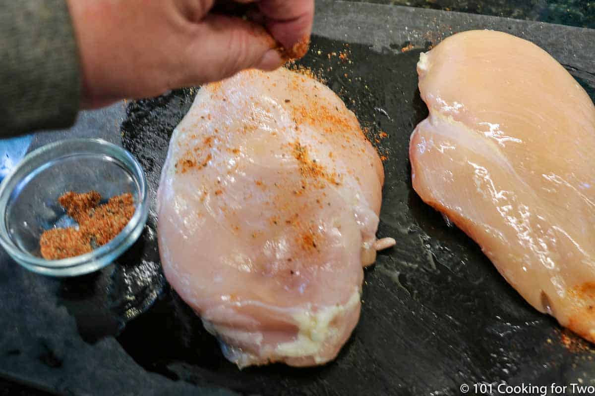 sprinkling spices on chicken breasts.