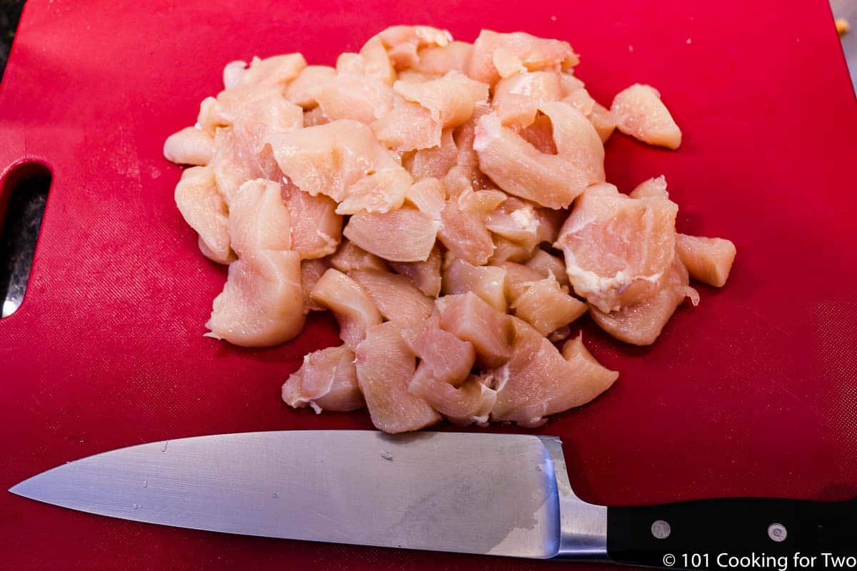 trimmed chicken with knife on a red board.