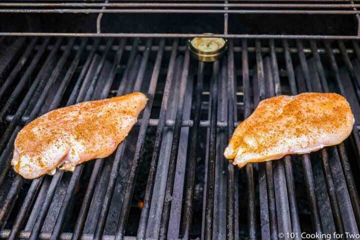 two raw seasoned chicken breasts on grill grates