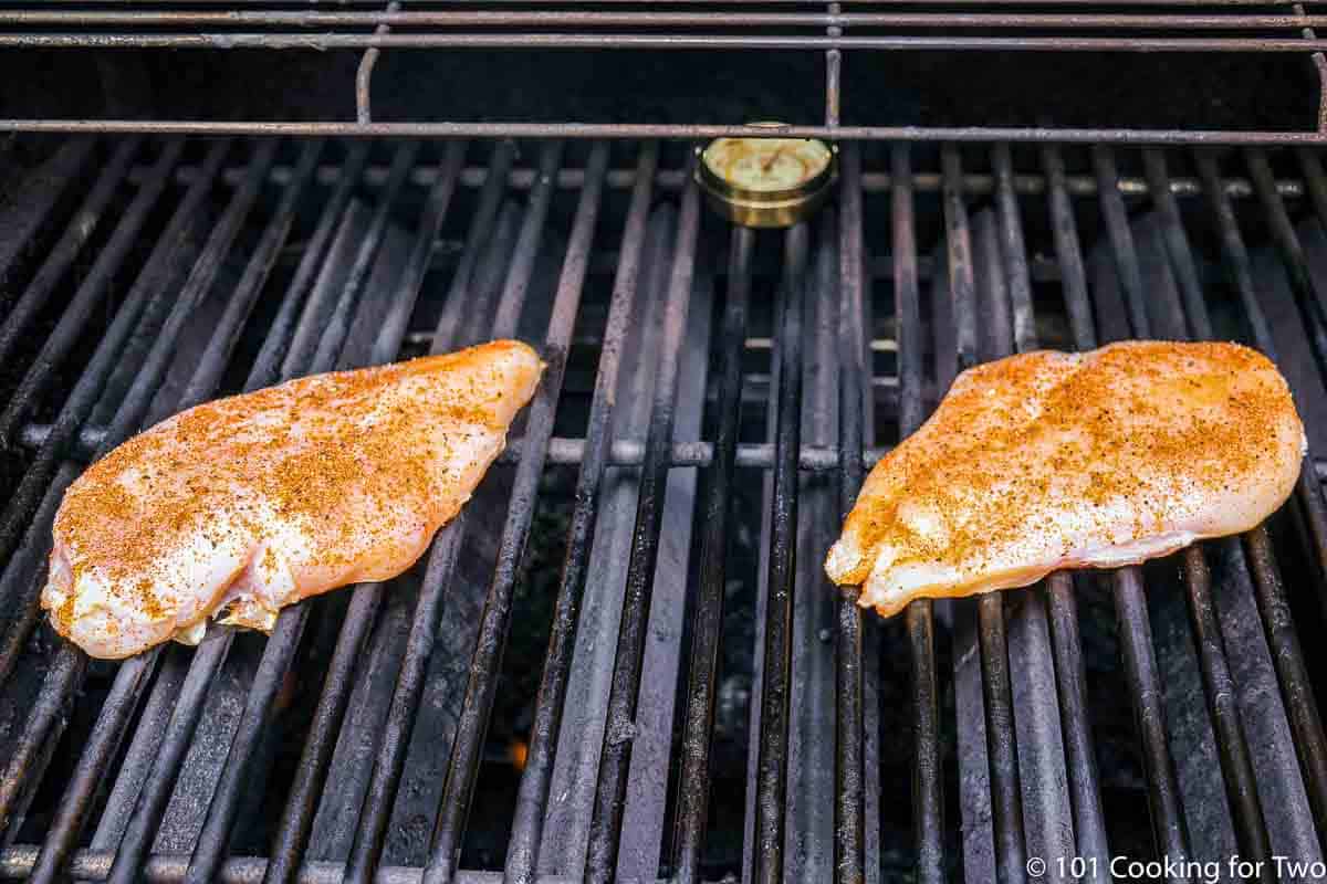 two raw seasoned chicken breasts on grill grates.