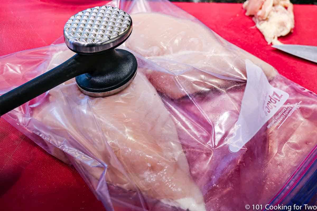 using a meat mallet on raw chicken in a zip lock bag