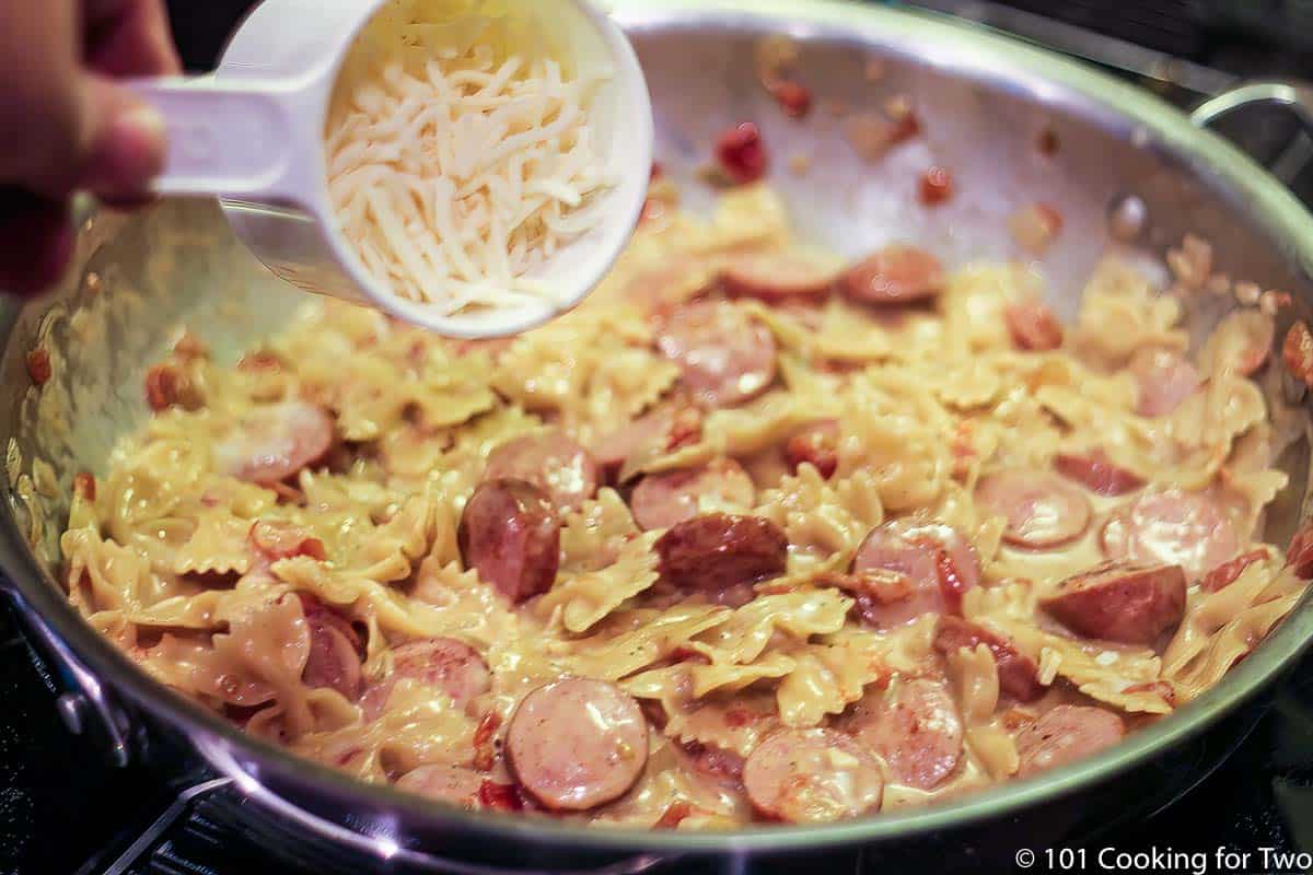 adding cheese to pasta in pan.