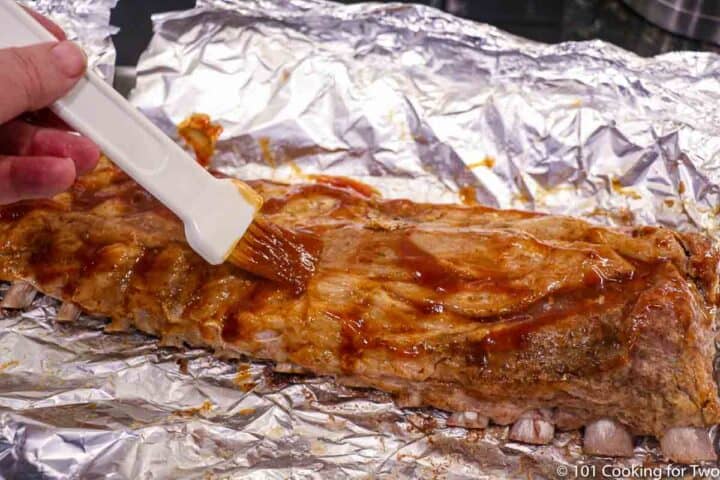 brushing BBQ sauce on cooked ribs