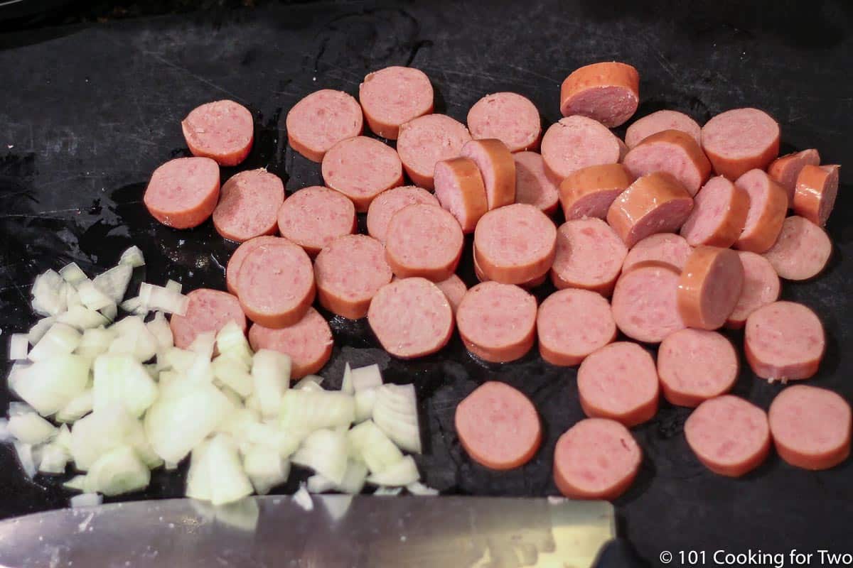 chopped onion and sliced smoked sausage on a black board.