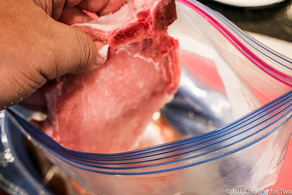 adding a pork chop to a bag with brine.