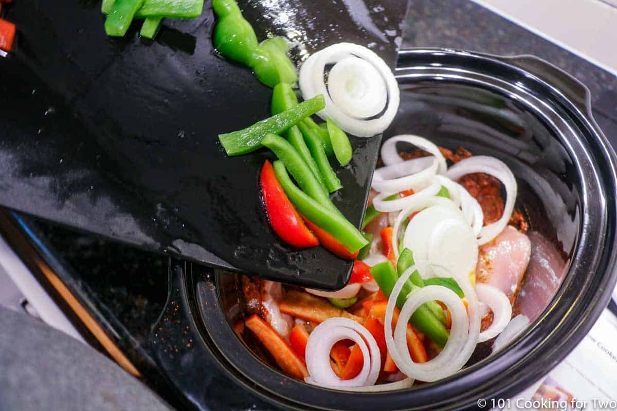 Adding vegetables into crock pot with chicken.