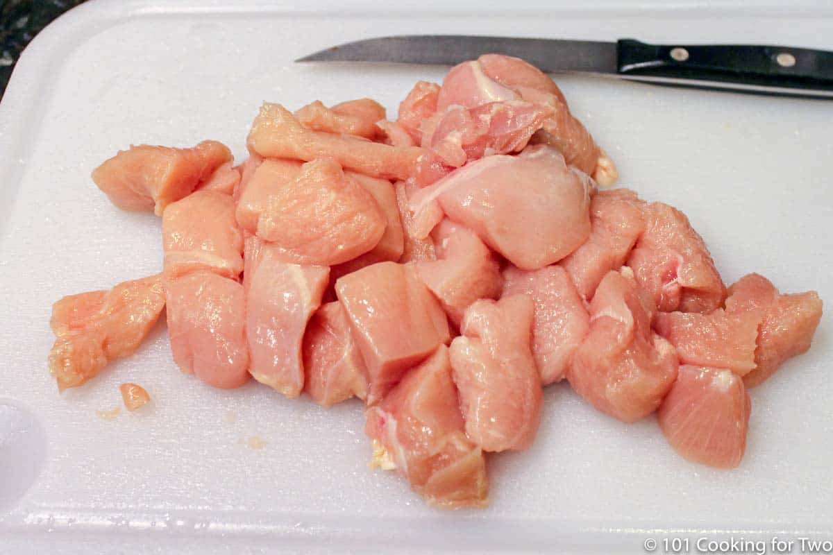 trimmed and cubed raw chicken on white board.