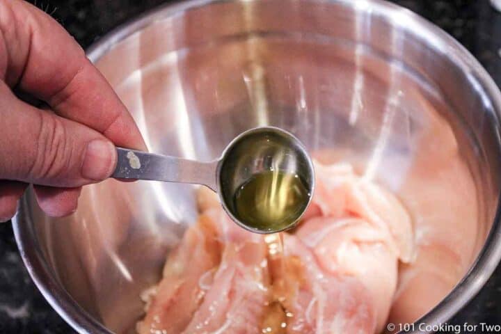 adding oil to chicken tenders in metal bowl