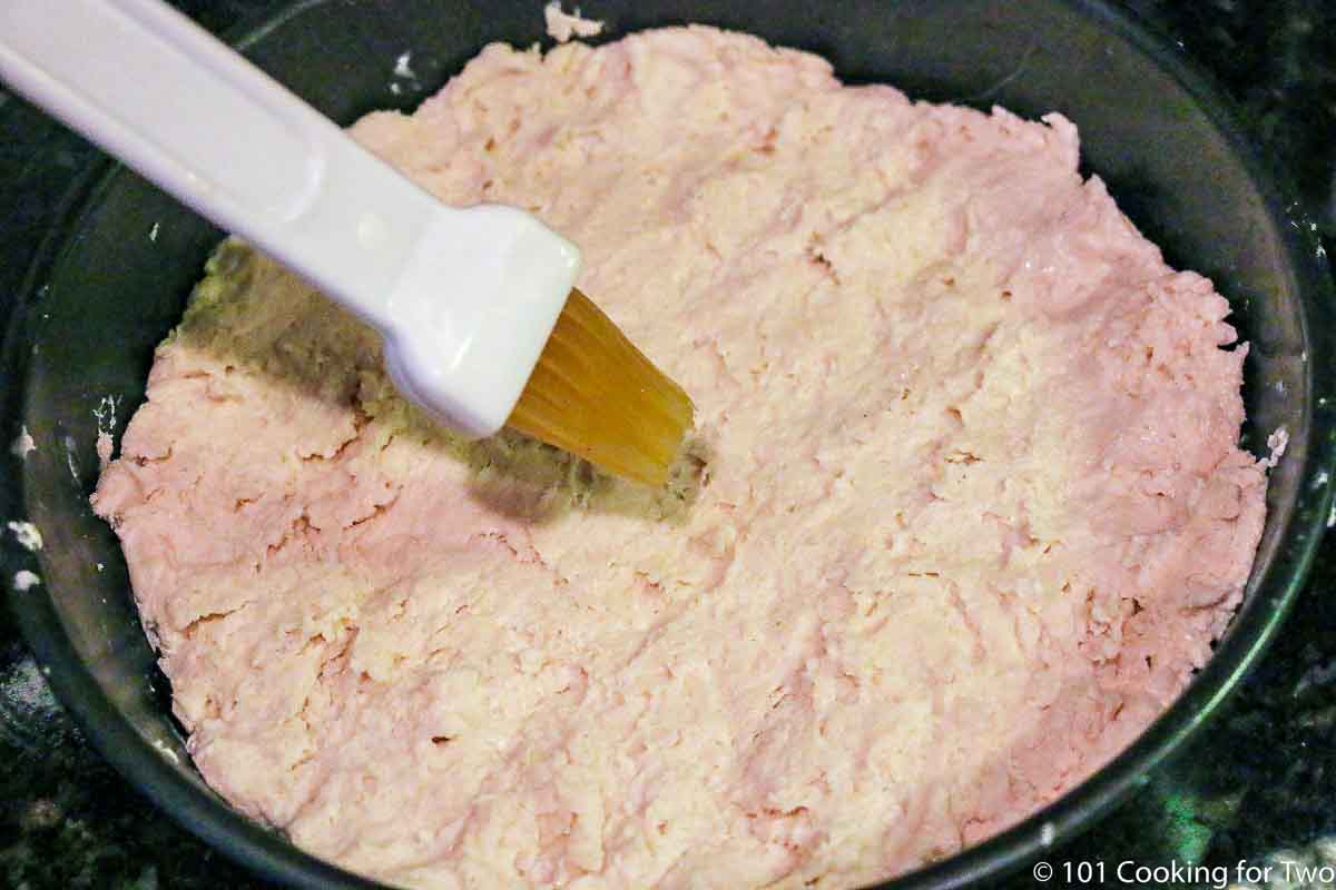 brushing biscuit crust with butter in pan
