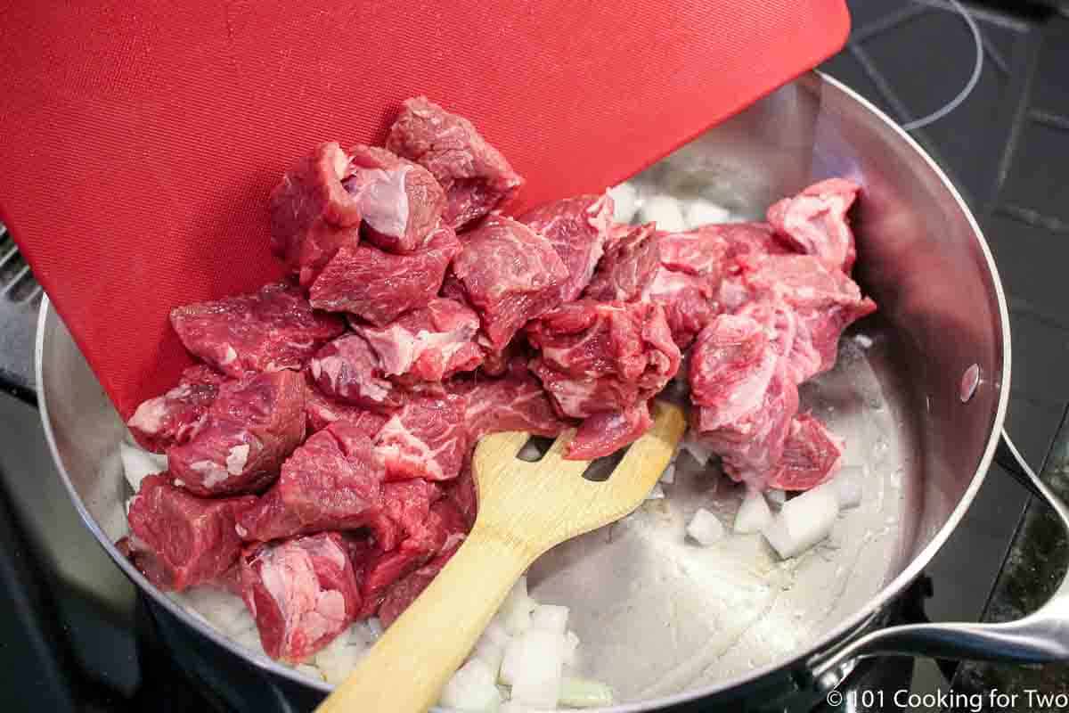 adding beef cubes to skillet with onion