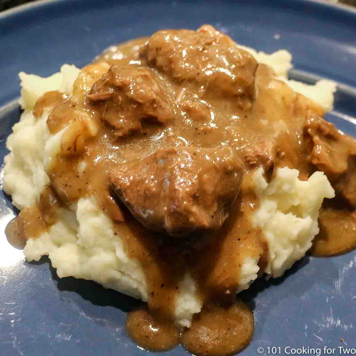beef tips in gravy on potatoes and blue plate