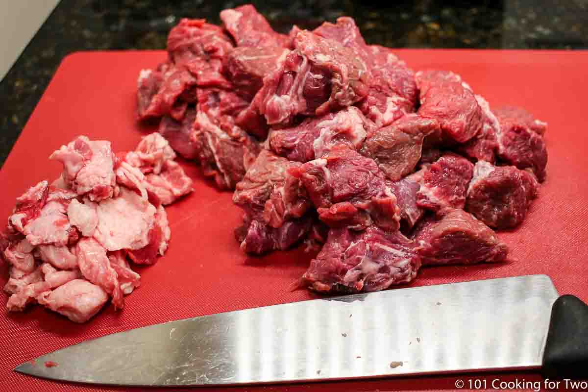 chuck roast trimmed of fat in cubes on a red board