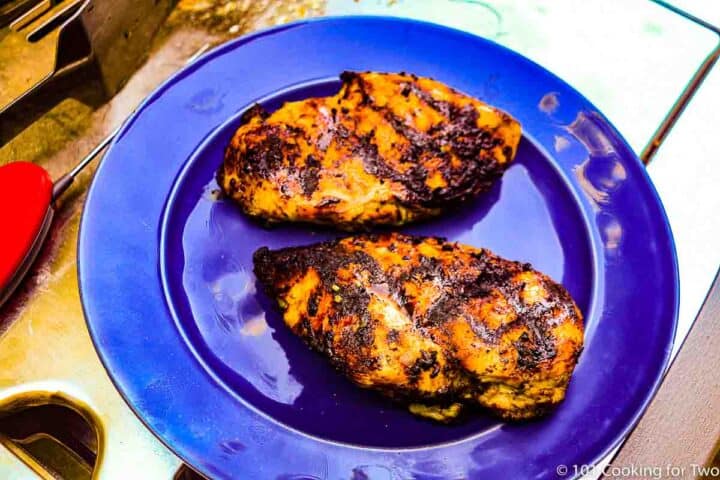 cooked chicken breasts on blue plate next to grill